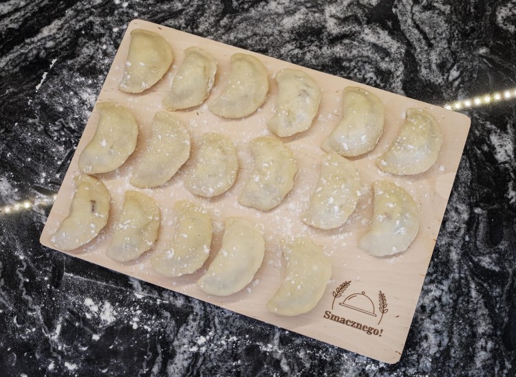 Drewniana deska z grawerem Smacznego, na której leżą pierogi