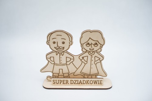 Drewniana statuetka z postaciami babci i dziadka jako super bohaterowie, przed nimi napis: super dziadkowie, figurka i napis na podstawce